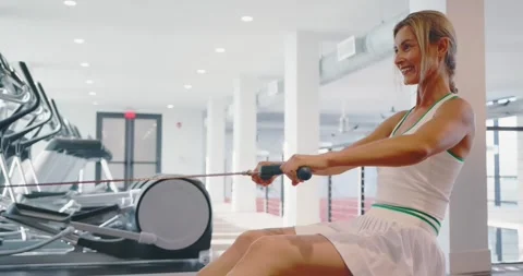 Woman Exercising on Rowing Machine in Modern Gym Stock Footage 323849174