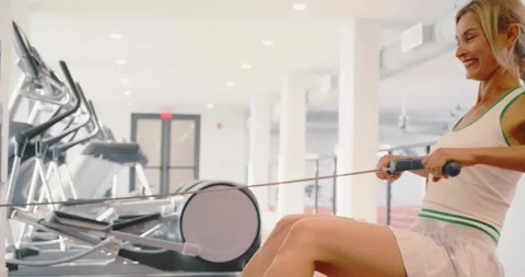 Woman Exercising on Rowing Machine in Modern Gym Stock Footage 323851310