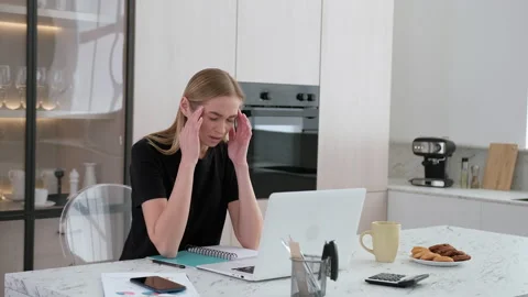 A woman experiences a headache while working at her desk at home. Stock Footage 253407744