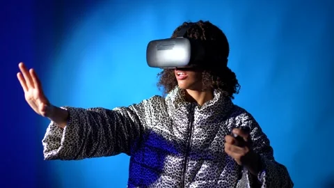 Woman exploring virtual reality with headset and controllers on blue background Stock Footage 301369824
