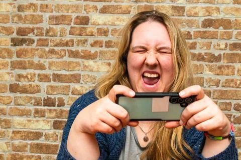 Woman expressing joy while taking a selfie against a rustic brick wall backdr Stock Photos