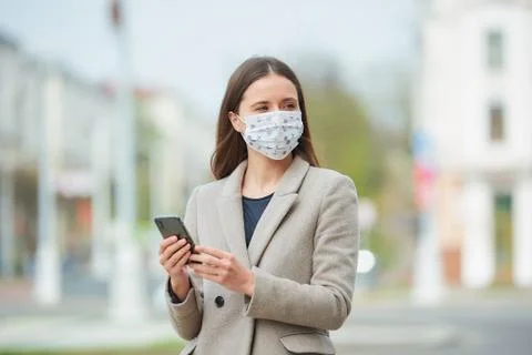 A woman in face mask to avoid the spread coronavirus uses a phone in the stre Stock Photos
