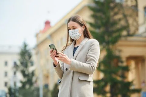 A woman in face mask to avoid the spread coronavirus uses a phone in the stre Stock Photos