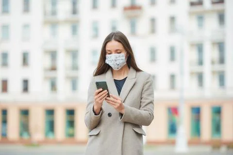 A woman in face mask to avoid the spread coronavirus uses a phone in the stre Stock Photos