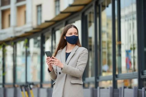 A woman in face mask to avoid the spread coronavirus uses a phone in the stre Stock Photos