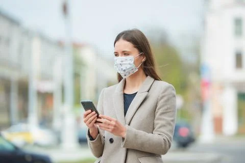 A woman in face mask to avoid the spread coronavirus uses a phone in the stre Stock Photos