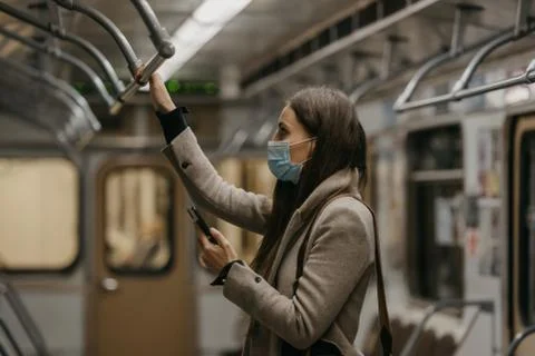A woman in face mask to avoid spread of coronavirus is using phone in subway  Stock Photos