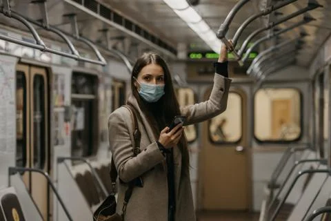 A woman in face mask to avoid spread of coronavirus is using phone in subway  Stock Photos