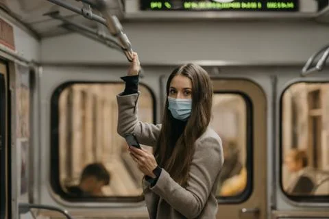 A woman in face mask to avoid spread of coronavirus is using phone in subway  Stock Photos