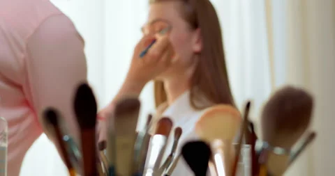 Woman face painter doing makeup to model girl through brushes foreground. Stock Footage 201366258