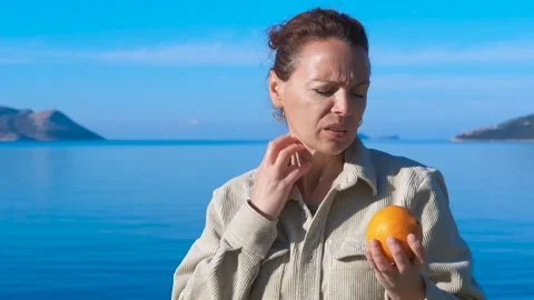 Woman feeling sick and refusing an orange by the sea Stock Footage 316079063