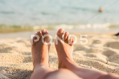 Woman feet on the sandy beach over sea in background. Stock Photos