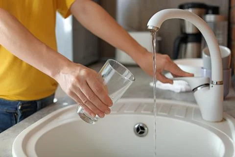 Woman filling glass with water from faucet in kitchen, closeup Stock Photos