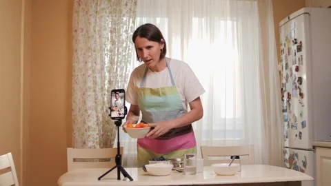 Woman filming cooking tutorial in kitchen on smartphone tripod Stock Footage 281689466