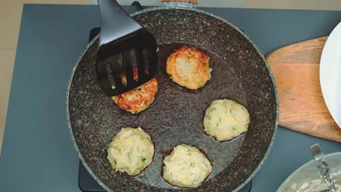 Woman flipping breaded vegetable cutlets in kitchen frying pan Stock Footage 342889422