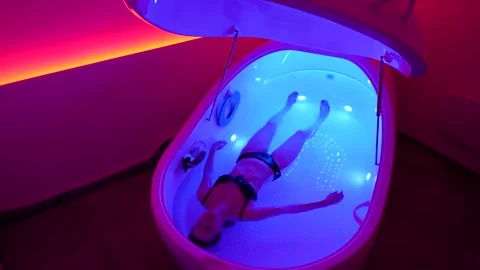 Woman float in relaxing hyper-saline floatation therapy pod in pink lit room Stock Footage 334043096