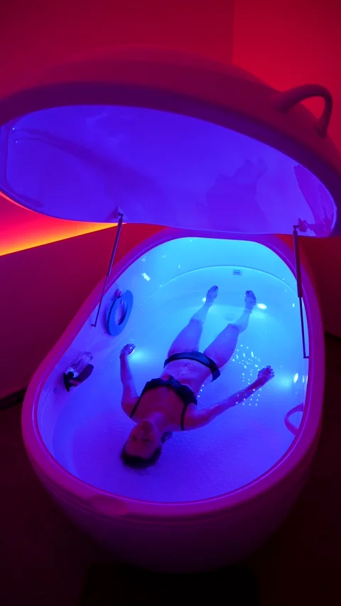 Woman float in relaxing hyper-saline floatation therapy pod in pink lit room Stock Footage 334043530