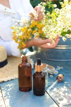 Woman with flowers near table outdoors, focus on bottles of chamomile essen.. Stock Photos