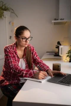 Woman focused on handwritten notes using laptop in the kitchen. Ideal for bus Stock Photos