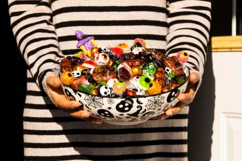 Woman at the front door offering Halloween candies on a nice bowl. Unrecogniz Stock Photos