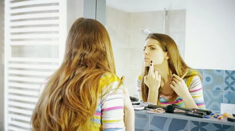 Woman in front of mirror finding pimple trying to cover it with makeup 4K Stock Footage 61806486