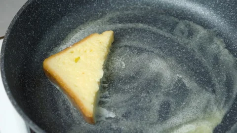 Woman frying bread slice in egg on frying pan cooking toasts on kitchen at home. Stock Footage 313133034