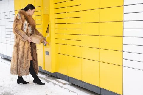 A woman in a fur coat types the code on the numeric keypad of a parcel locker Stock Photos