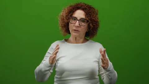 Woman gesturing calmly against a solid green wall background, expressing co.. Stock Footage 312345510