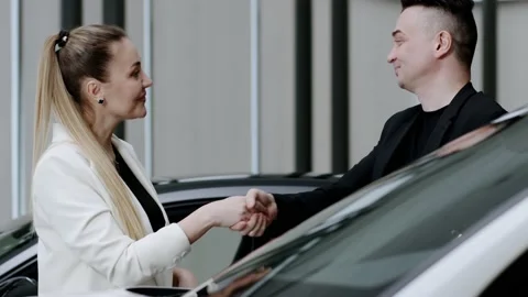 Woman gives keys to a new electric car to a man client in the showroom Stock Footage