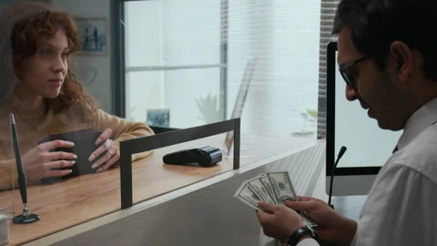 Woman Giving Stack of American Dollar Bills to Bank Teller Stock Footage 310128239