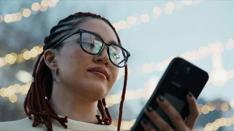 Woman with glasses and dreadlocks using phone outdoors at night with bokeh Stock Footage 341330141