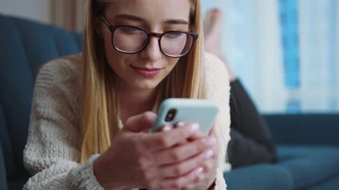 Woman with glasses lying on sofa using smartphone in modern room. Feel happy Stock Footage 147001440
