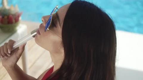 Woman in glasses smokes hookah while releasing smoke while sitting near the pool Stock Footage 200811330