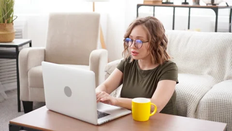 Woman glasses using laptop computer while sitting near sofa with big window on Stock Footage 155275982