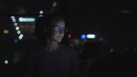 Woman in glasses using the tablet pc and drinking tea beside the window at night Video stock 88100490