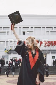 Woman in graduation gown holding mortarboard while standing against building Stock Photos