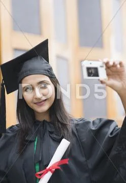 Woman in graduation gown taking a picture of herself with a digital camera Stock Photos