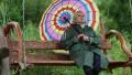 Woman in green raincoat and with umbrella sits on the swing bench HD Footage