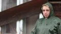 Woman in green raincoat stands near uninhabited house HD Footage
