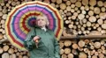 Woman in green raincoat with umbrella stands near wooden logs HD Footage