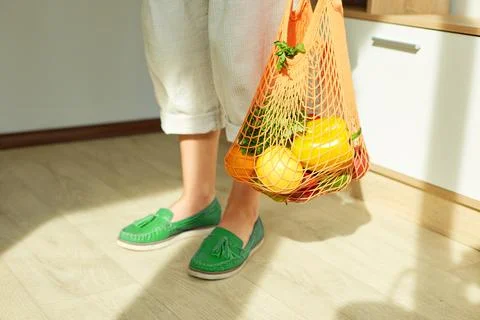 Woman in green shoes holding string grocery reusable mesh bag full of fresh f Stock Photos