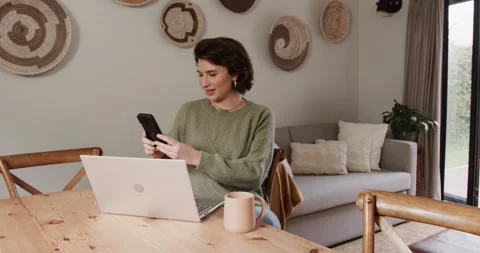 Woman in green sweater reading confusing phone message at desk before typing Stock Footage 336957413