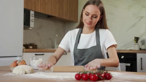 Woman in a grey chef's apron roll out the dough for preparing pancake. Woman 스톡 동영상 211630341