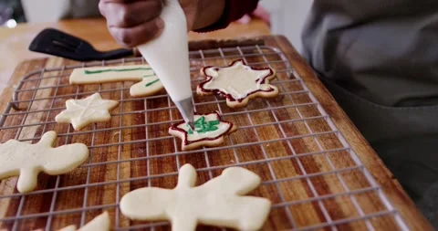 Woman guiding piping bag, adding green Christmas design on cookie at counter, Stock Footage 344228787