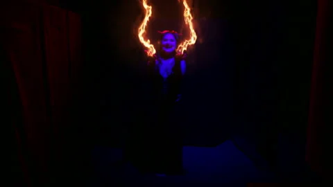 A woman in the guise of a devil is dancing with fire burning in her arms 動画素材 121017467