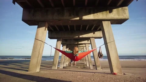 Woman in hammock under pier at beach Stock Footage