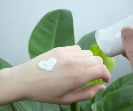 Woman hand applies hand cream on skin, green leaves background Stock Photos