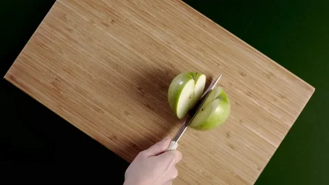 Woman hand is cutting fresh green apple on a wooden surface Stock Footage