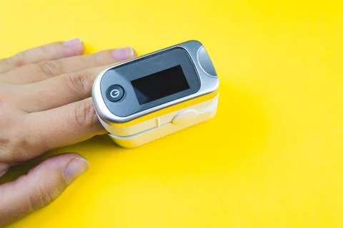 Woman hand with a finger in pulse oximeter on yellow background. Stock Photos