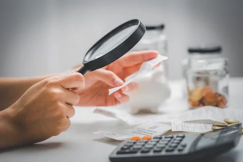 Woman hand holding magnifying glass to check receipts to calculate expenses.  Stock Photos